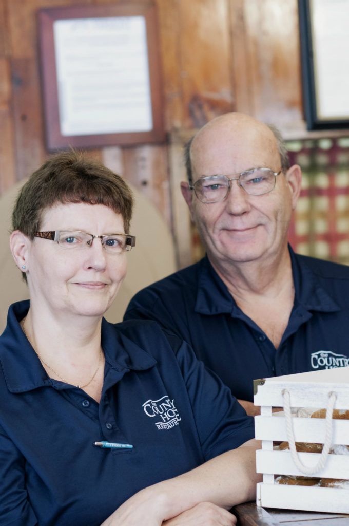 A man and a woman with glasses in blue shirts standing in a restaurant The Country House