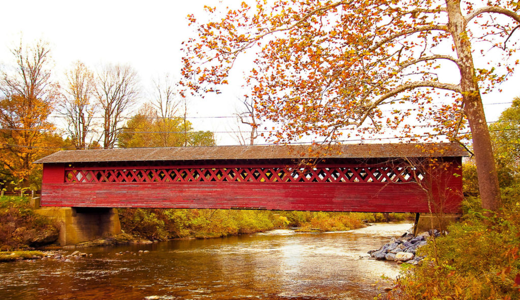 A beautiful red covered bridge spanning a serene creek, taken in the fall
